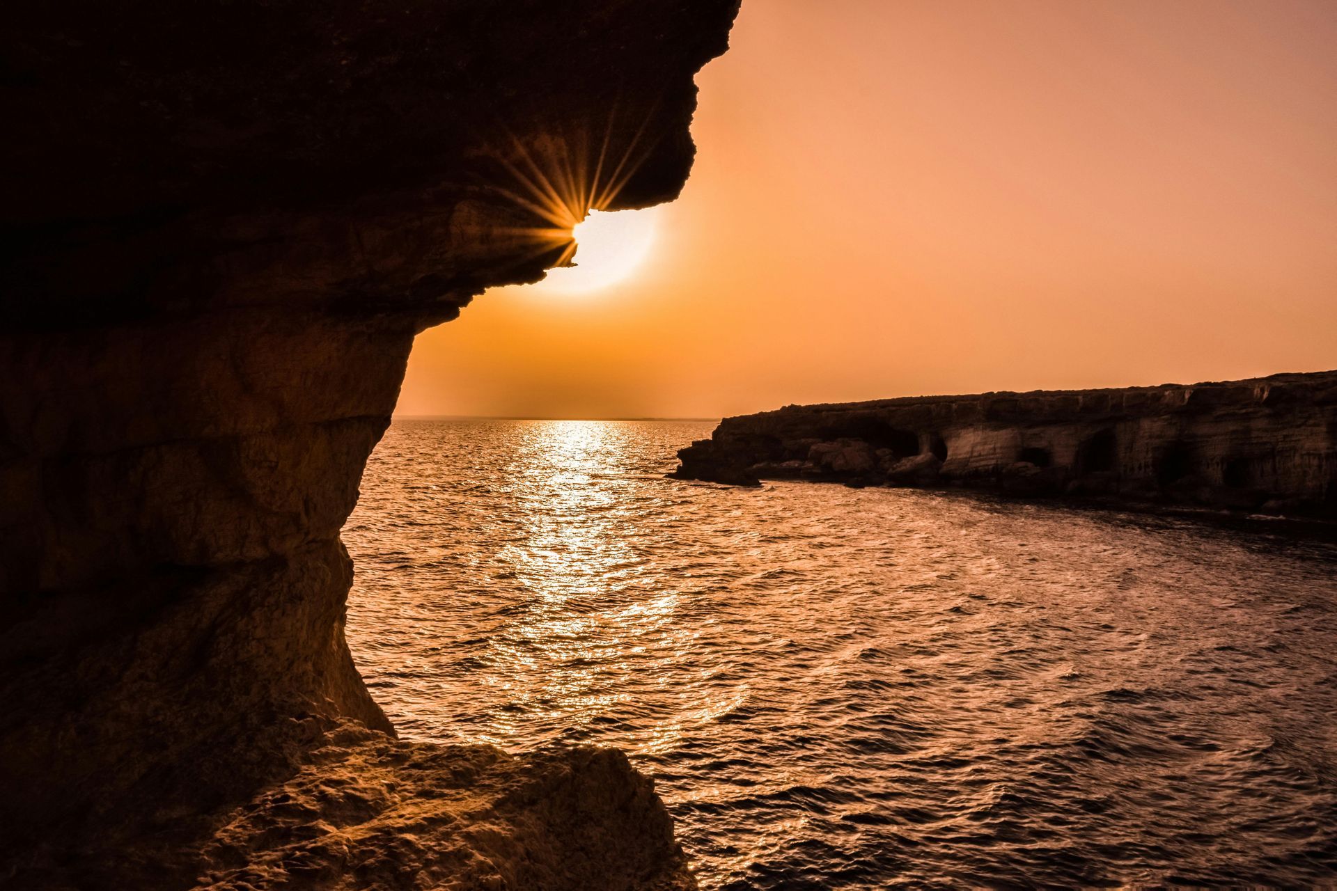 The sun is setting over the ocean in a cave.
