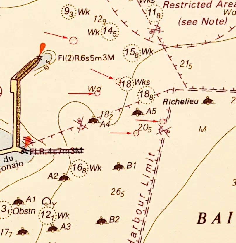 Sección de la carta náutica que muestra sondeos de profundidad, símbolos de naufragios, una línea de límite del puerto y balizas de luces de navegación.