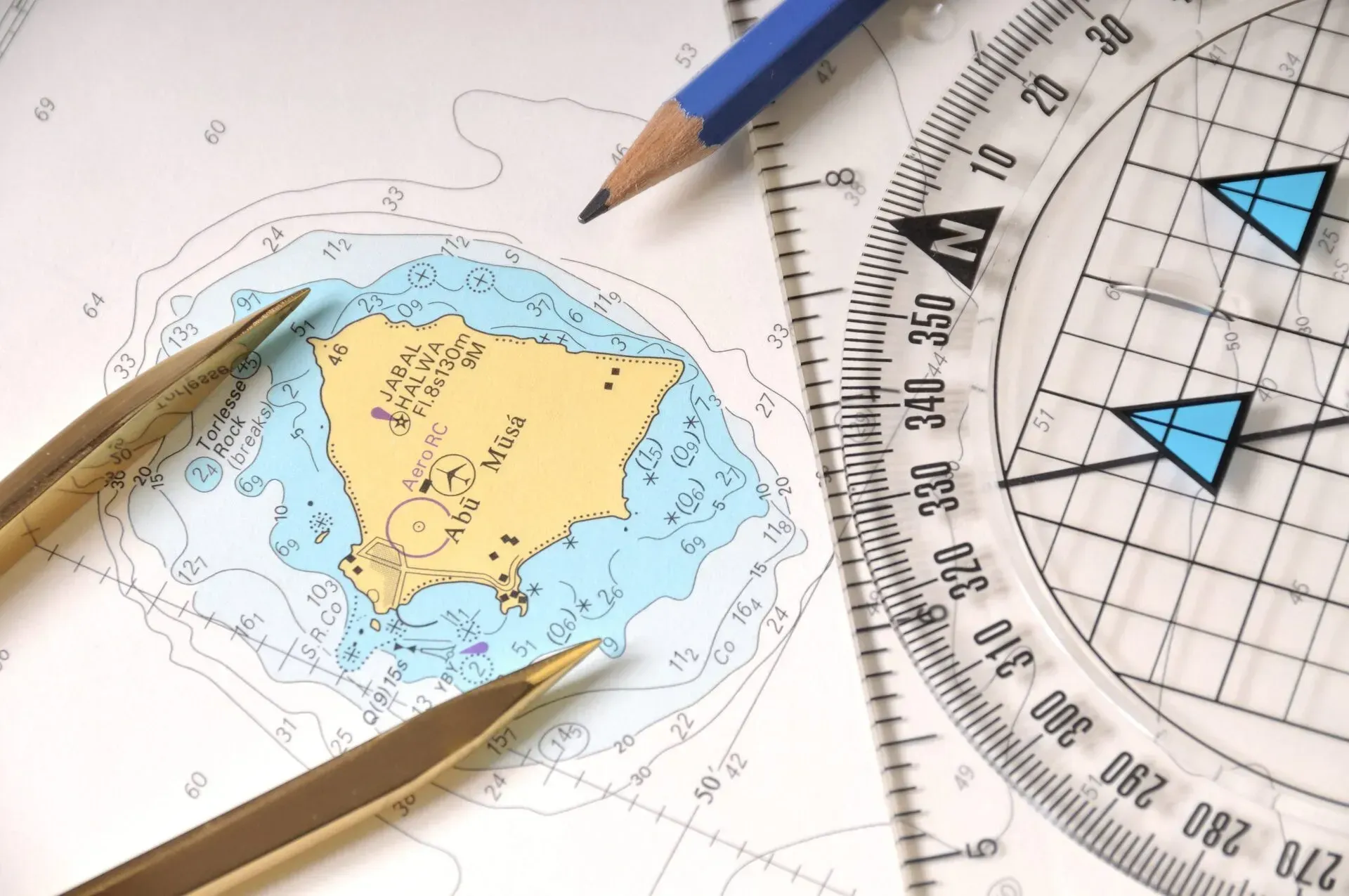 Una carta náutica de una isla sobre una mesa con un compás, un transportador y un lápiz, que muestra la planificación de la navegación.