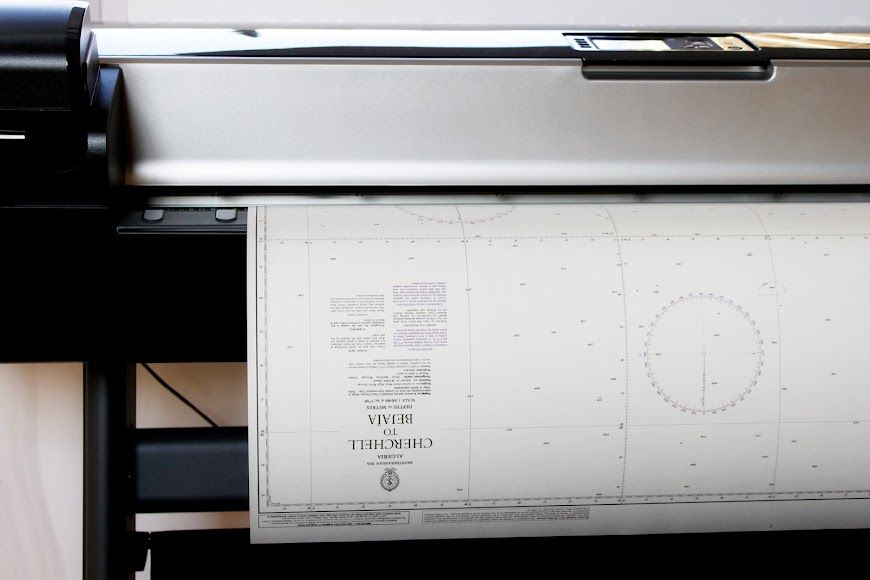 Coche gris cerca de una puerta metálica abierta, de listones horizontales, y de un muro de piedra en un día soleado.