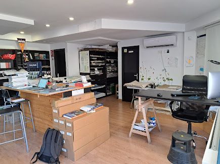 Una oficina desordenada con suelo de madera, escritorios, pilas de cajas, estanterías, una silla con ruedas y un aire acondicionado montado en la pared.