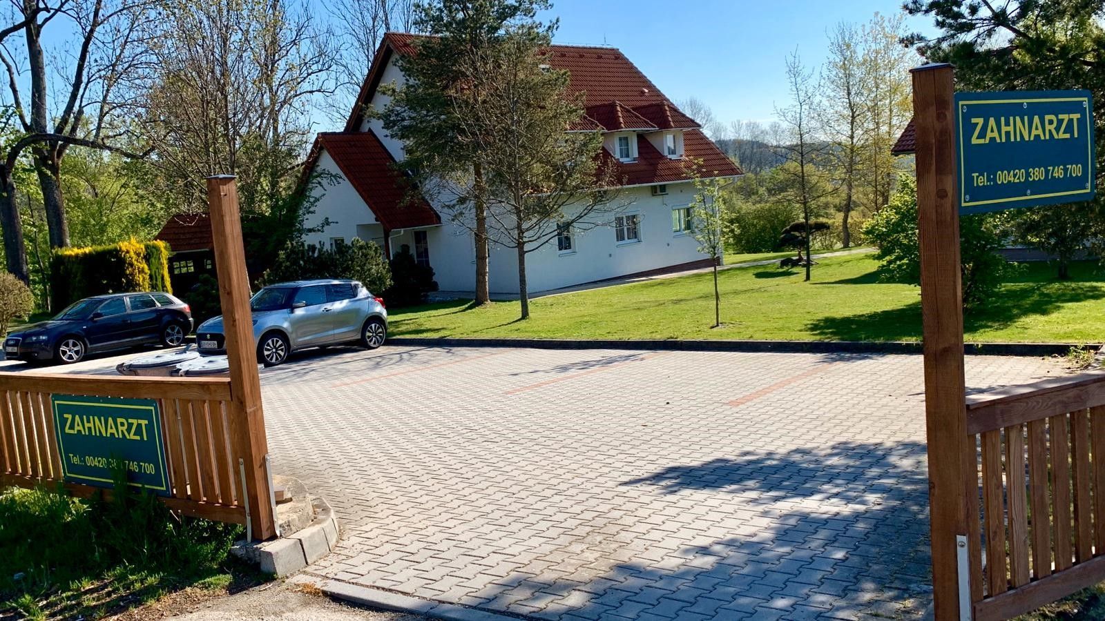 Hinter einem Holztor befindet sich ein weißes Haus mit rotem Dach.