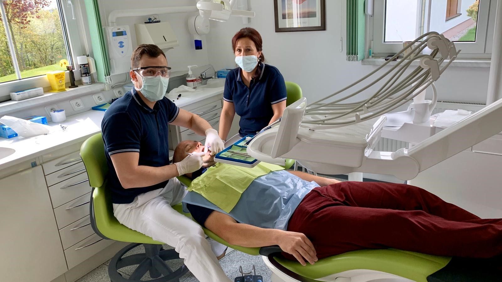Ein Mann liegt in einem Zahnarztstuhl, während zwei Zahnärzte zuschauen.