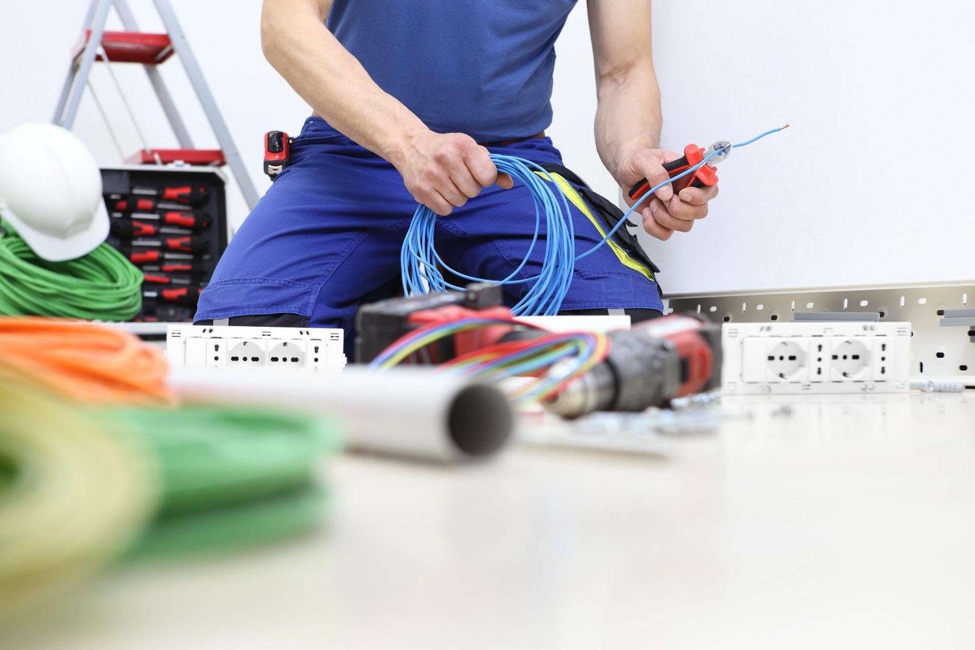 Electricista colocando cables cerca de una regleta en un banco de trabajo, con herramientas y cables enrollados.