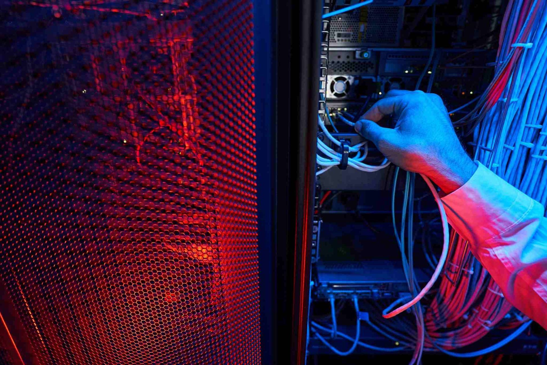 Un técnico conecta cables dentro de un rack de servidores, iluminado por luces rojas y azules.