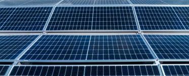Filas de paneles solares azules dispuestos en cuadrícula bajo la luz brillante del sol.