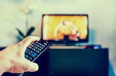 Una mano que sostenía un control remoto negro apuntaba a una pantalla de televisión azul borrosa.