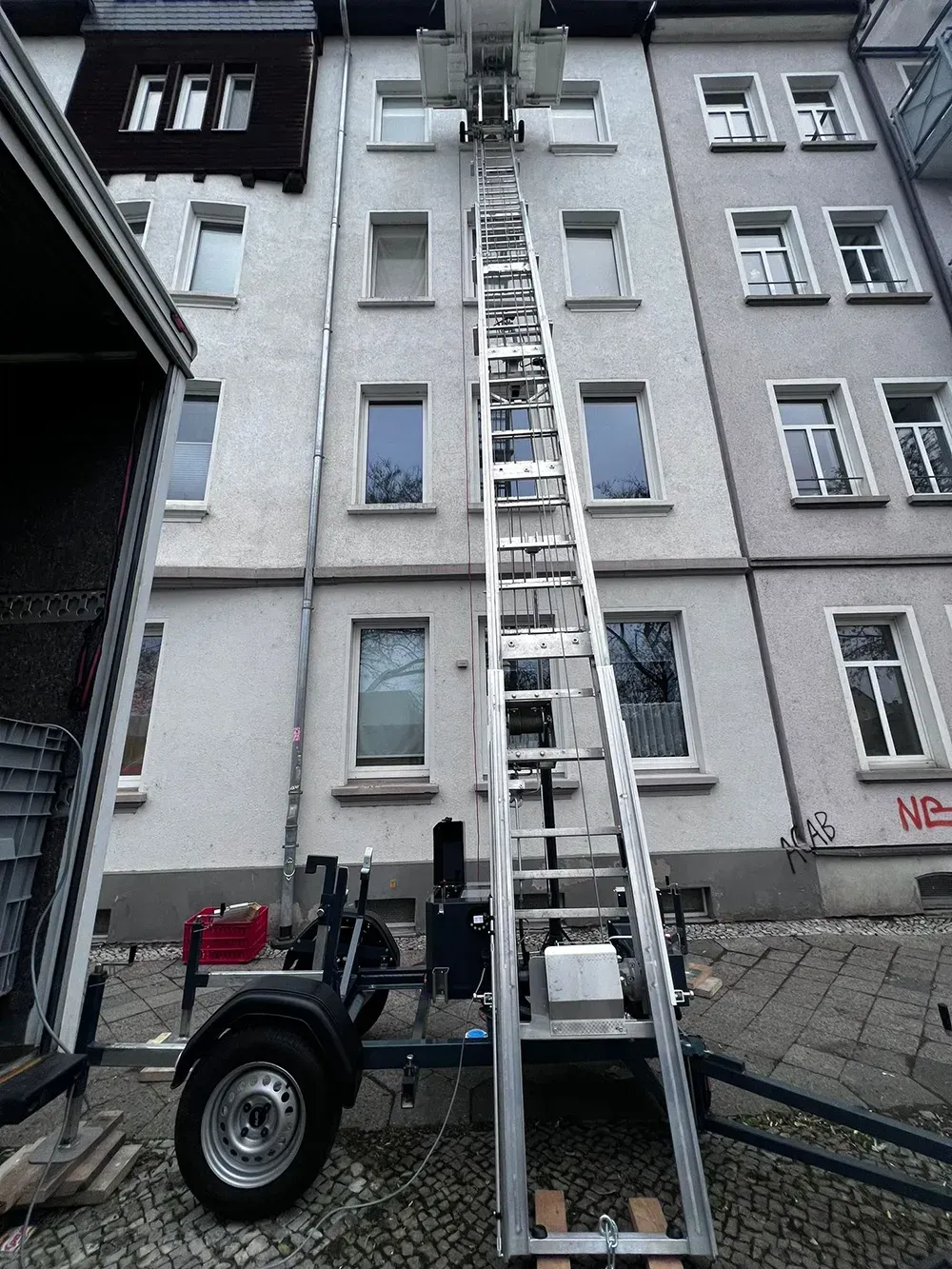 Ein Möbellift steht an einer Hauswand und transportiert Möbel nach oben Ein Möbellift steht an einer Hauswand und transportiert Möbel nach oben