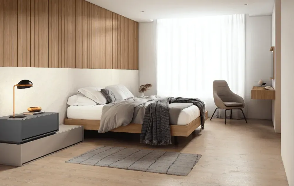 Un dormitorio con una cama, mesita de noche, silla y ventana.