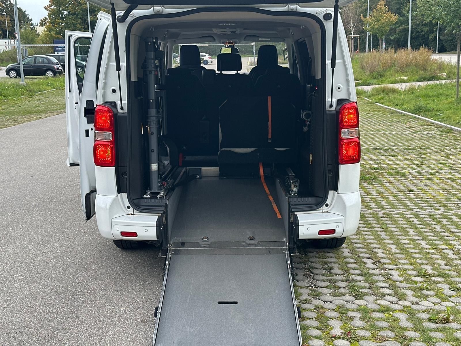 Die Hand einer Person am Rad eines Rollstuhls in einem hell erleuchteten Flur.