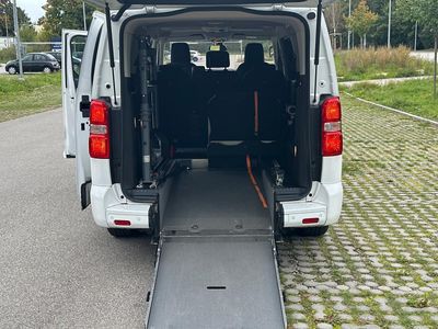 Die Hand einer Person am Rad eines Rollstuhls in einem hell erleuchteten Flur.