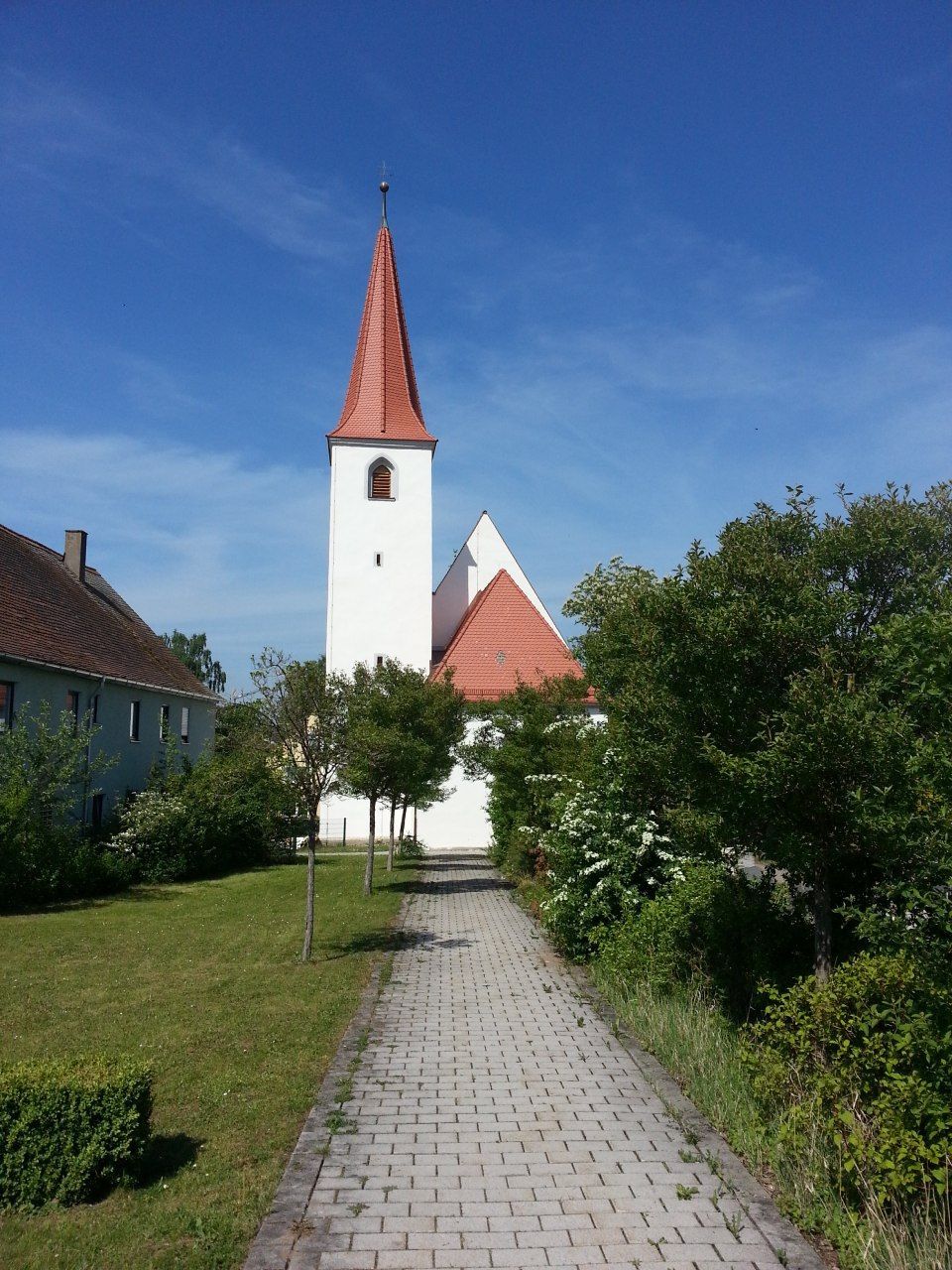 Weiße Kirche mit rotem Kirchturm am Ende eines Kopfsteinpflasterwegs an einem sonnigen Tag