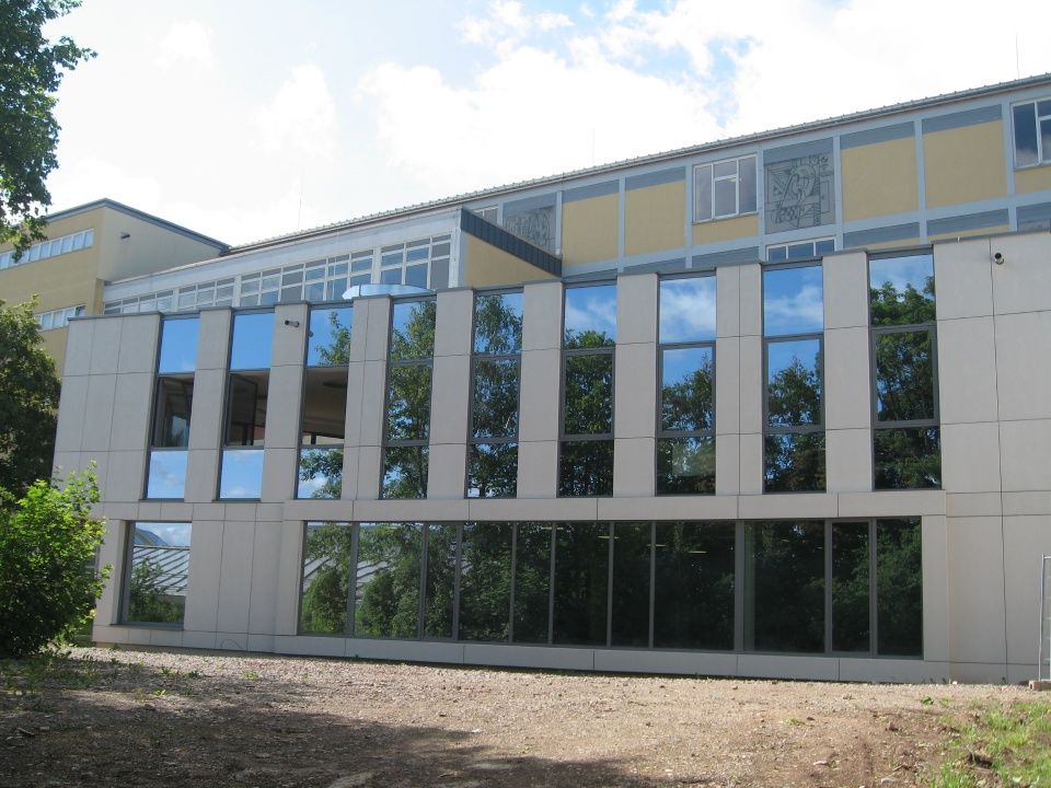 Moderne Gebäudefassade mit großen, reflektierenden Fenstern und beigefarbenen Paneelen unter blauem Himmel