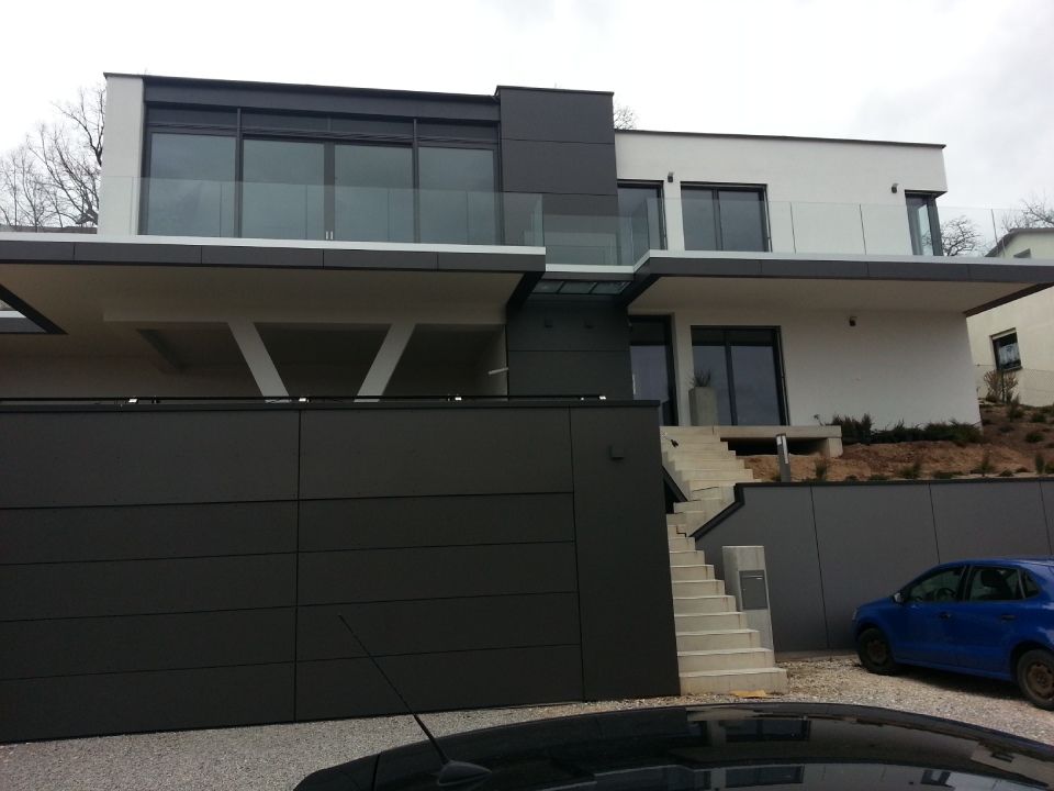Modernes zweistöckiges Haus mit dunklen Garagentoren und einem blauen Auto, das in der Einfahrt parkt.