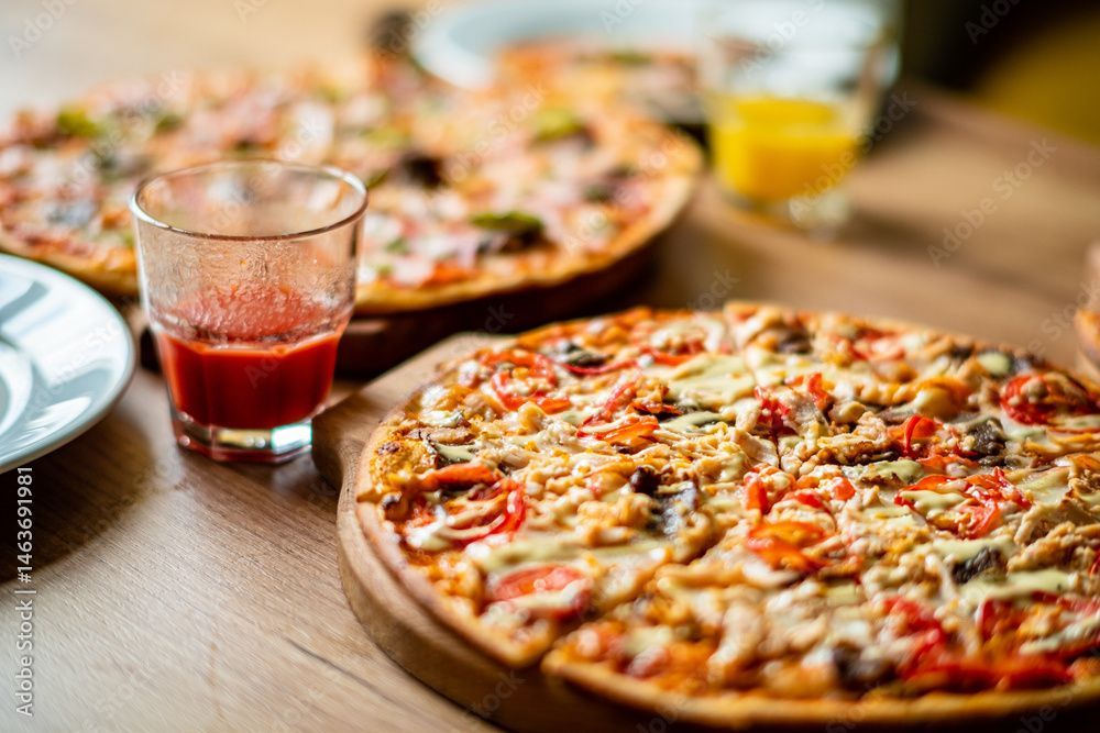 Des pizzas sur des planches en bois, un verre de jus et un verre de liquide rouge sur une table en bois.