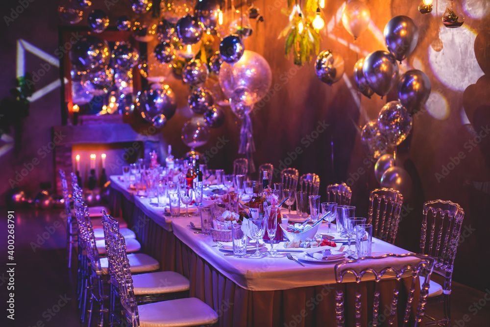 Table de dîner formelle dressée avec des ballons argentés, des bougies et des chaises en cristal.