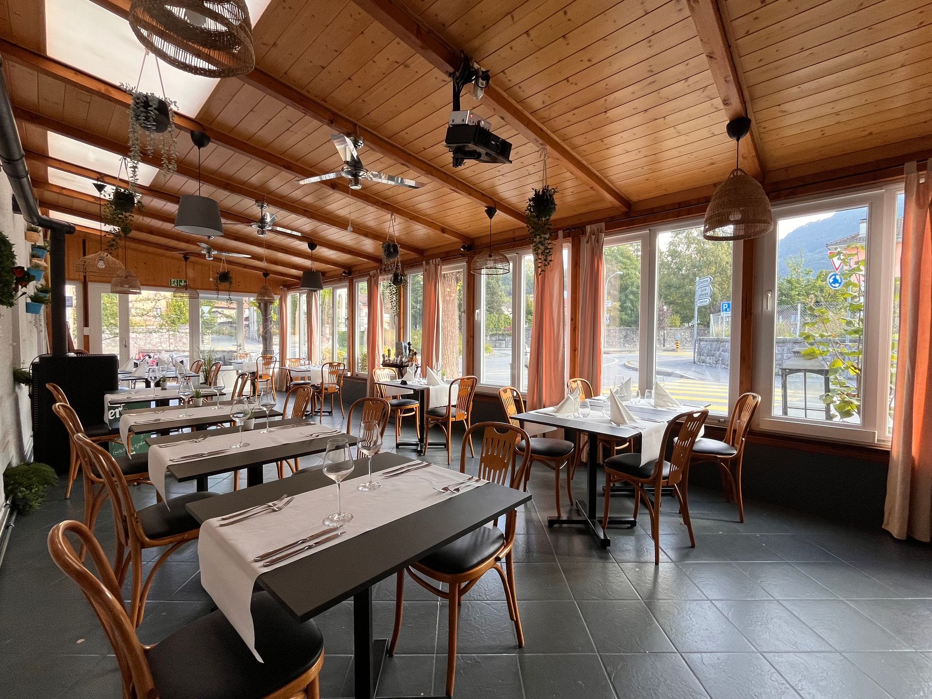 Intérieur de restaurant avec tables dressées pour manger, fenêtres, plafond en bois et chaises.