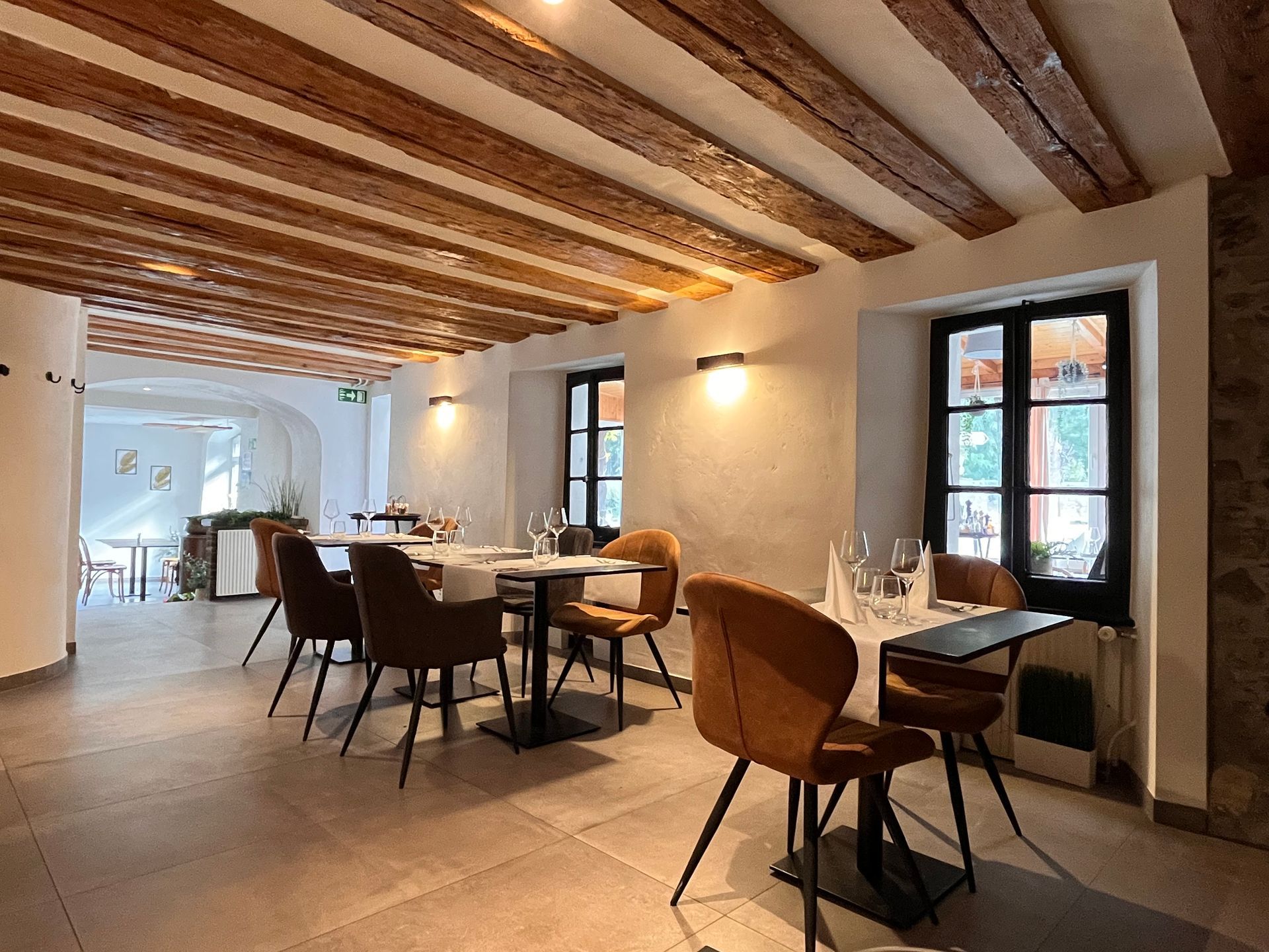 Intérieur de restaurant avec poutres, tables, chaises et fenêtres marron.