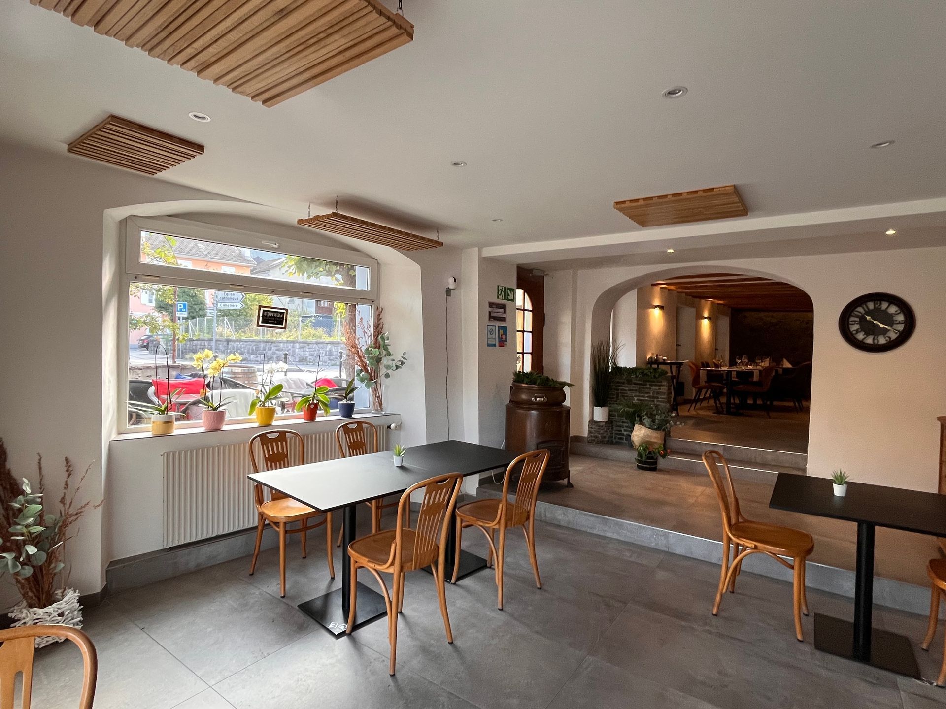 Intérieur d'un restaurant avec tables et chaises, grande fenêtre donnant sur une rue et accents en bois.