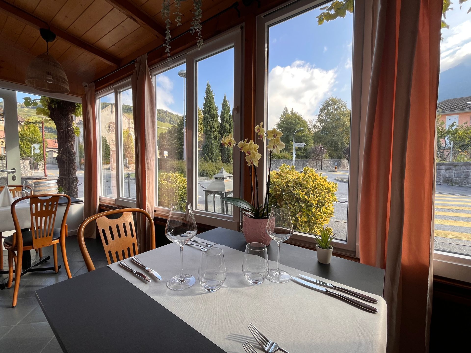 Tables de restaurant en plein air dressées avec assiettes, verres et couverts, prêtes à être servies.