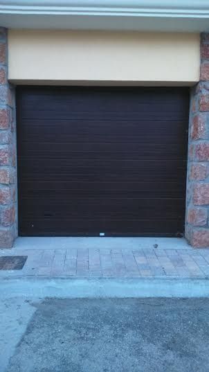 Una puerta de garaje marrón está al lado de una pared de ladrillos.