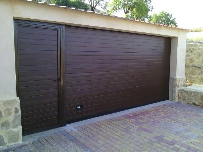 Una puerta de garaje marrón con un camino de entrada de ladrillos delante de ella.