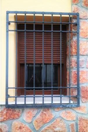 Una ventana con una reja de hierro forjado está en una pared de ladrillos.