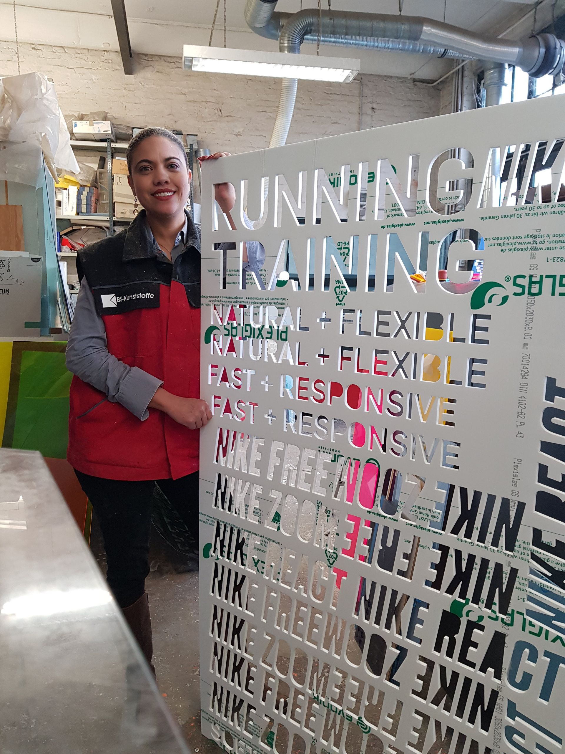 Mitarbeiterin vor einem Glas- oder Acrylschild mit dem Schriftzug „RUNNING TRAINING“.