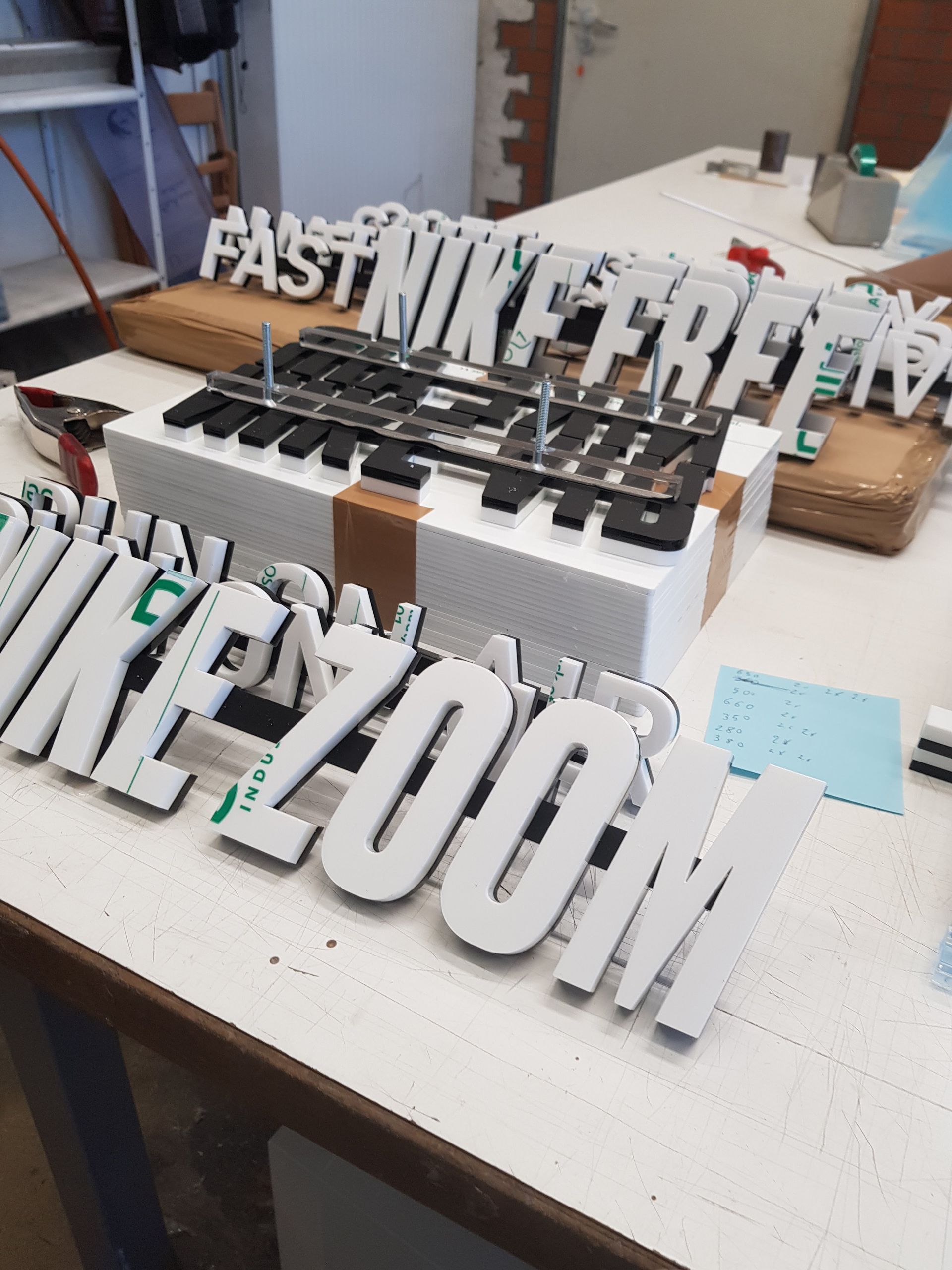 Metallische Einzelbuchstaben für einen Schriftzug, auf Abstandshaltern auf einer Werkbank montiert.