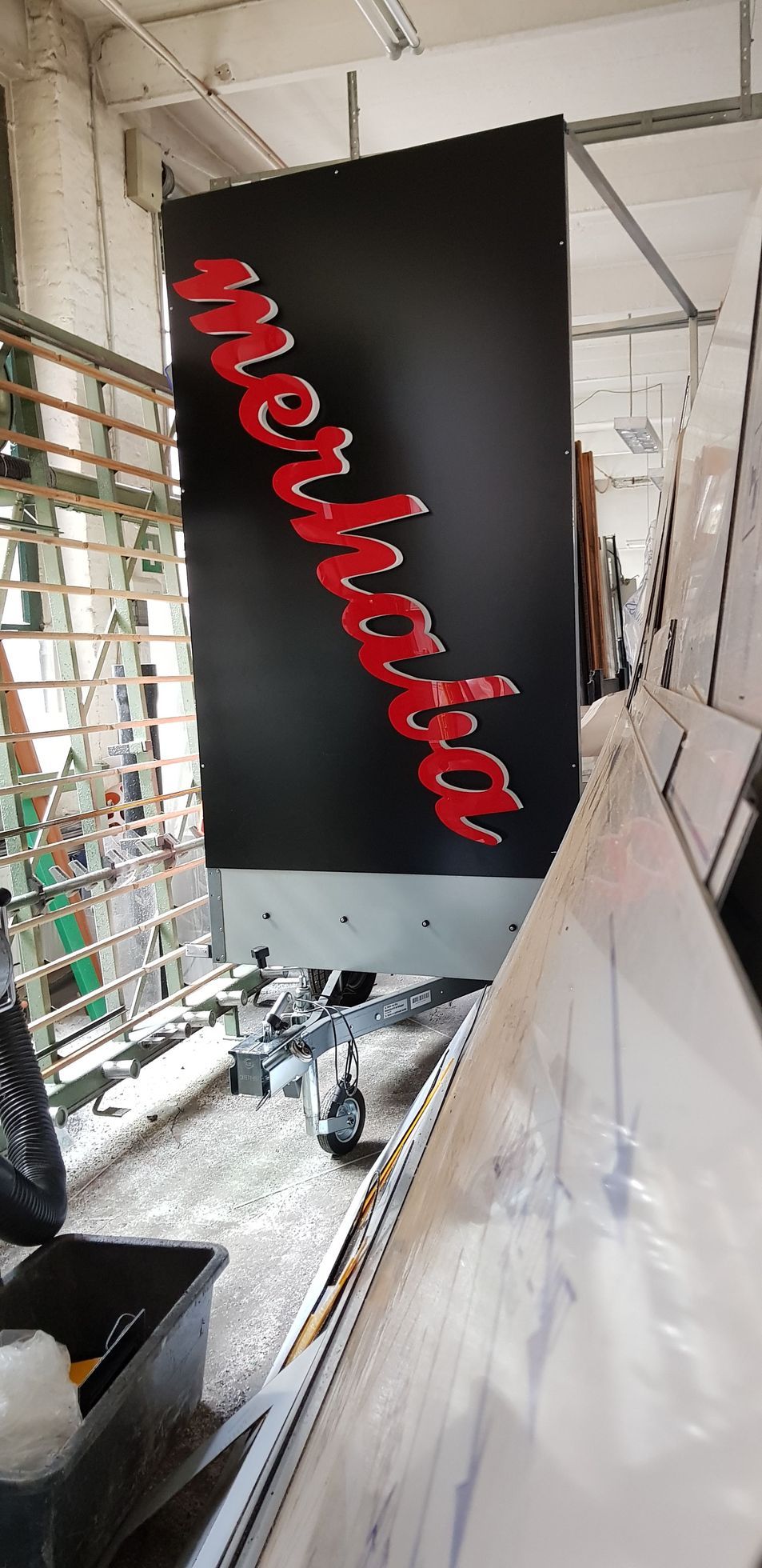 Schwarze Platte mit rotem, geschwungenem Schriftzug, hängend in einer Werkstatt.