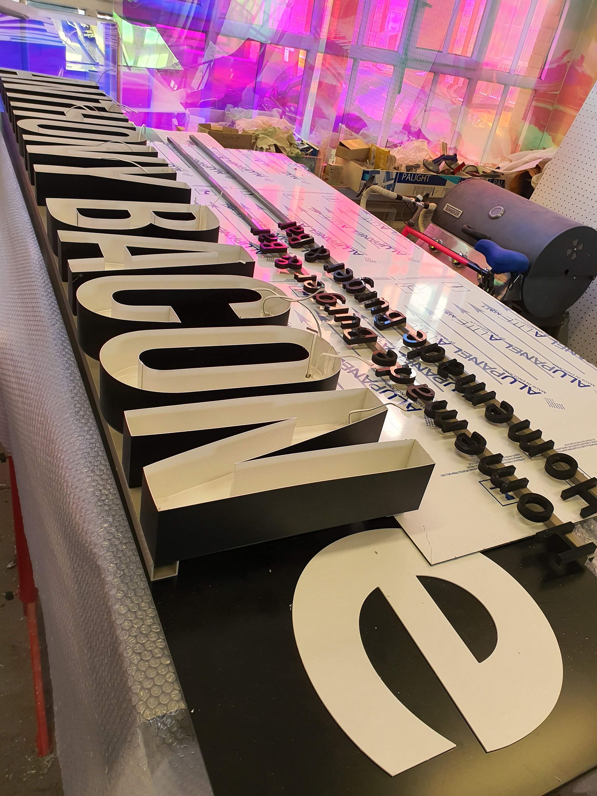 Perspektivische Ansicht eines Schriftzuges aus schwarzen Buchstaben unter farbigem Licht.