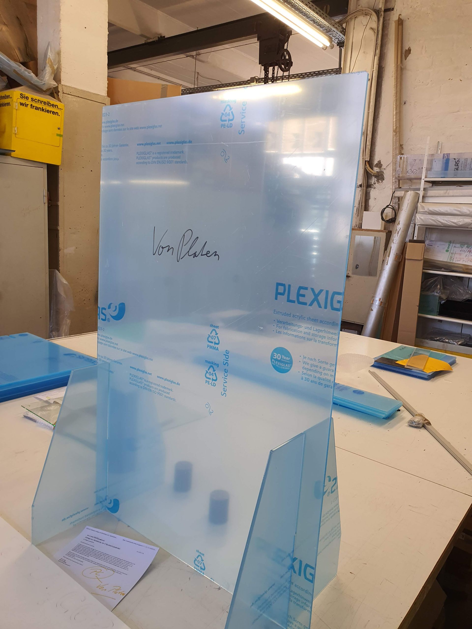 Große, transparente Kunststoffplatte mit handschriftlichen Markierungen in einer Werkstatt.