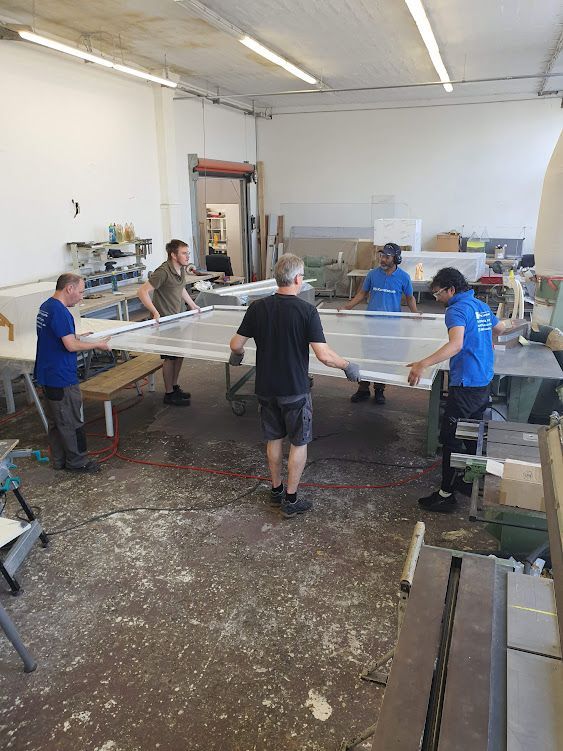 Team arbeitet gemeinsam an großen Werkbänken in einer hellen Werkstatt.