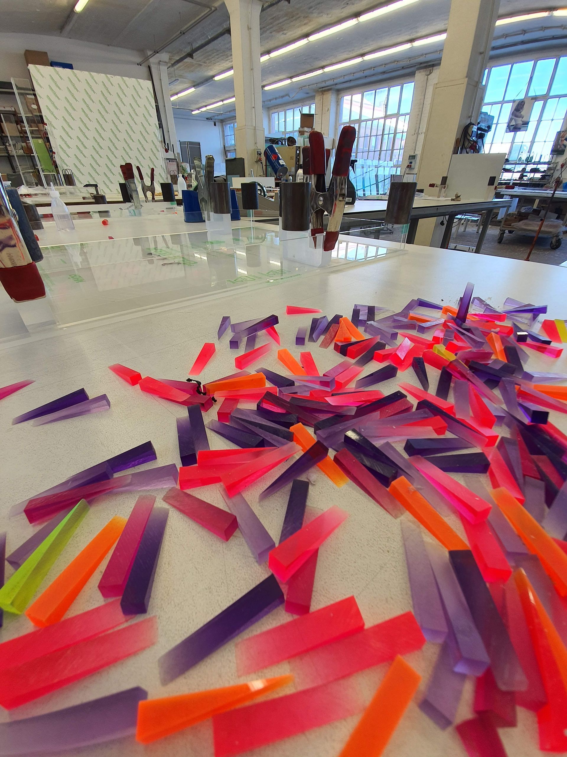 Große Werkhalle mit Arbeitstischen, transparenten Objekten und mehreren Personen im Hintergrund.