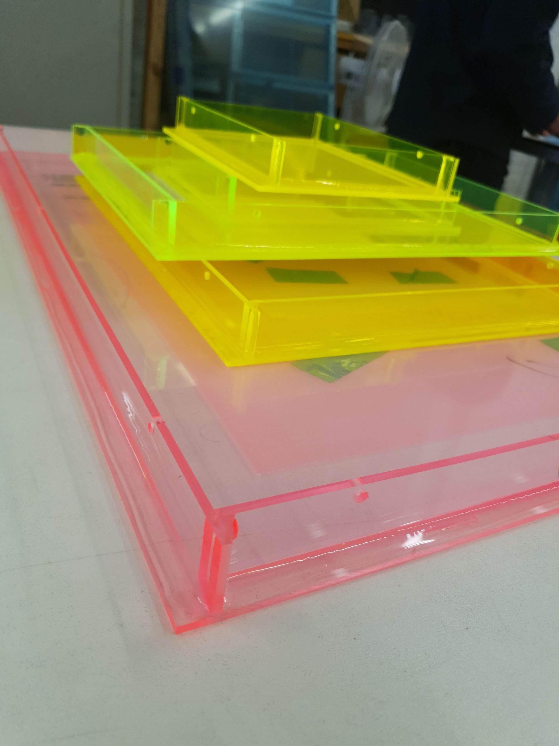 Mehrschichtige, transparente Acrylplatten in Gelb und Grün, gestapelt auf einer Arbeitsfläche.