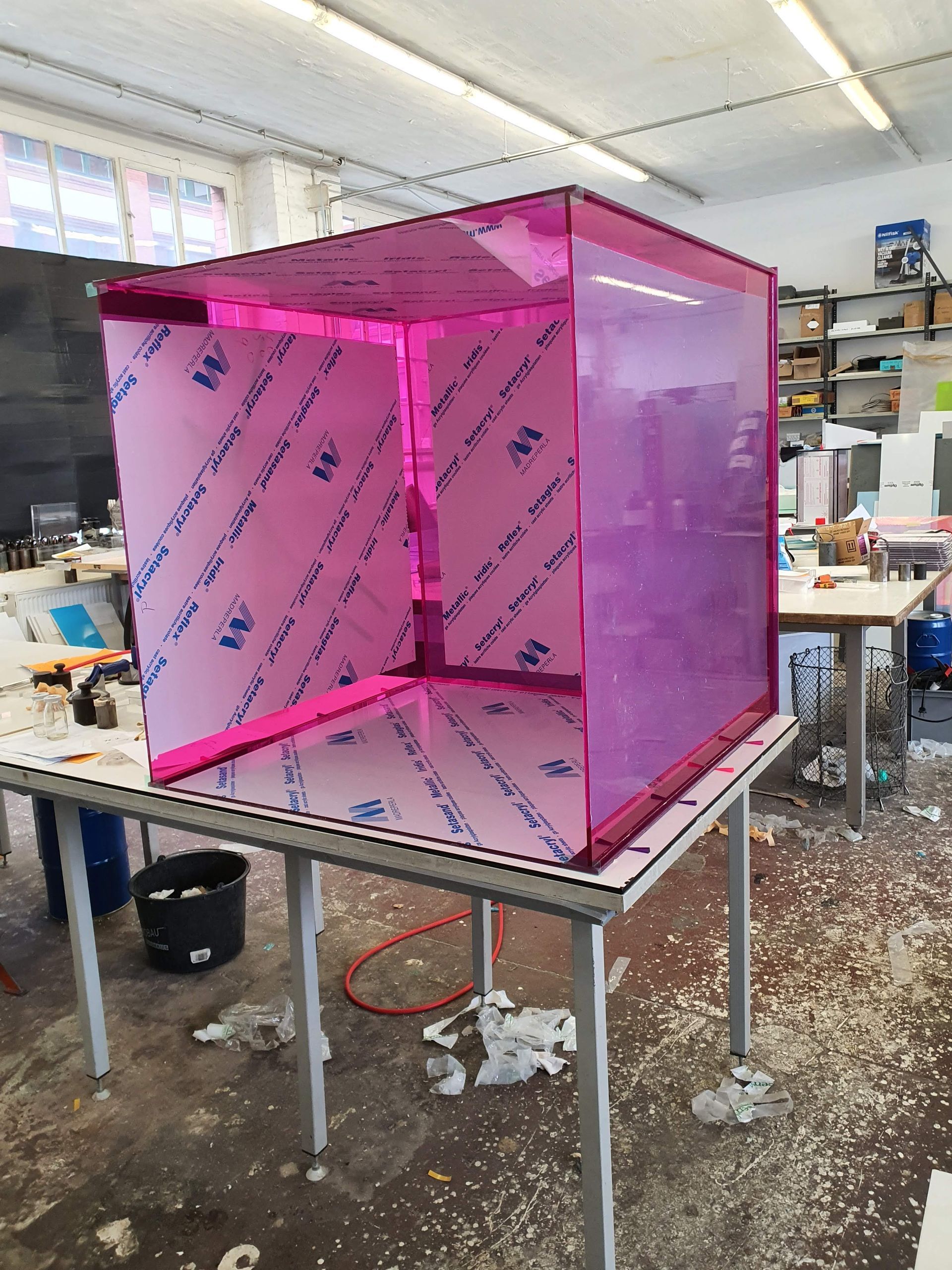 Würfelförmiges Objekt aus pinkfarbenem, transparentem Kunststoff in einer Werkstatt.