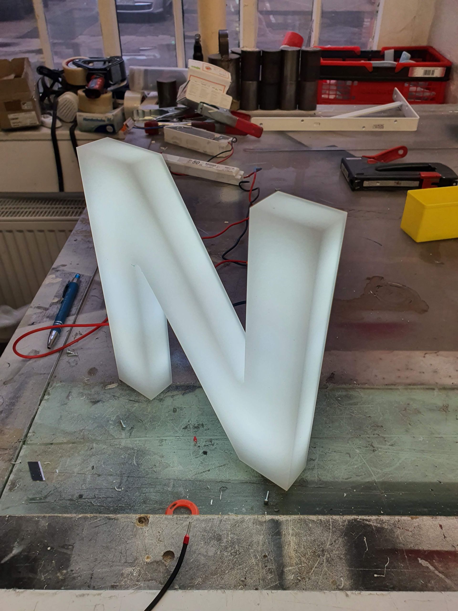 Werkbank mit Werkzeugen, Kabeln und Materialien zur Herstellung von Leuchtschildern.