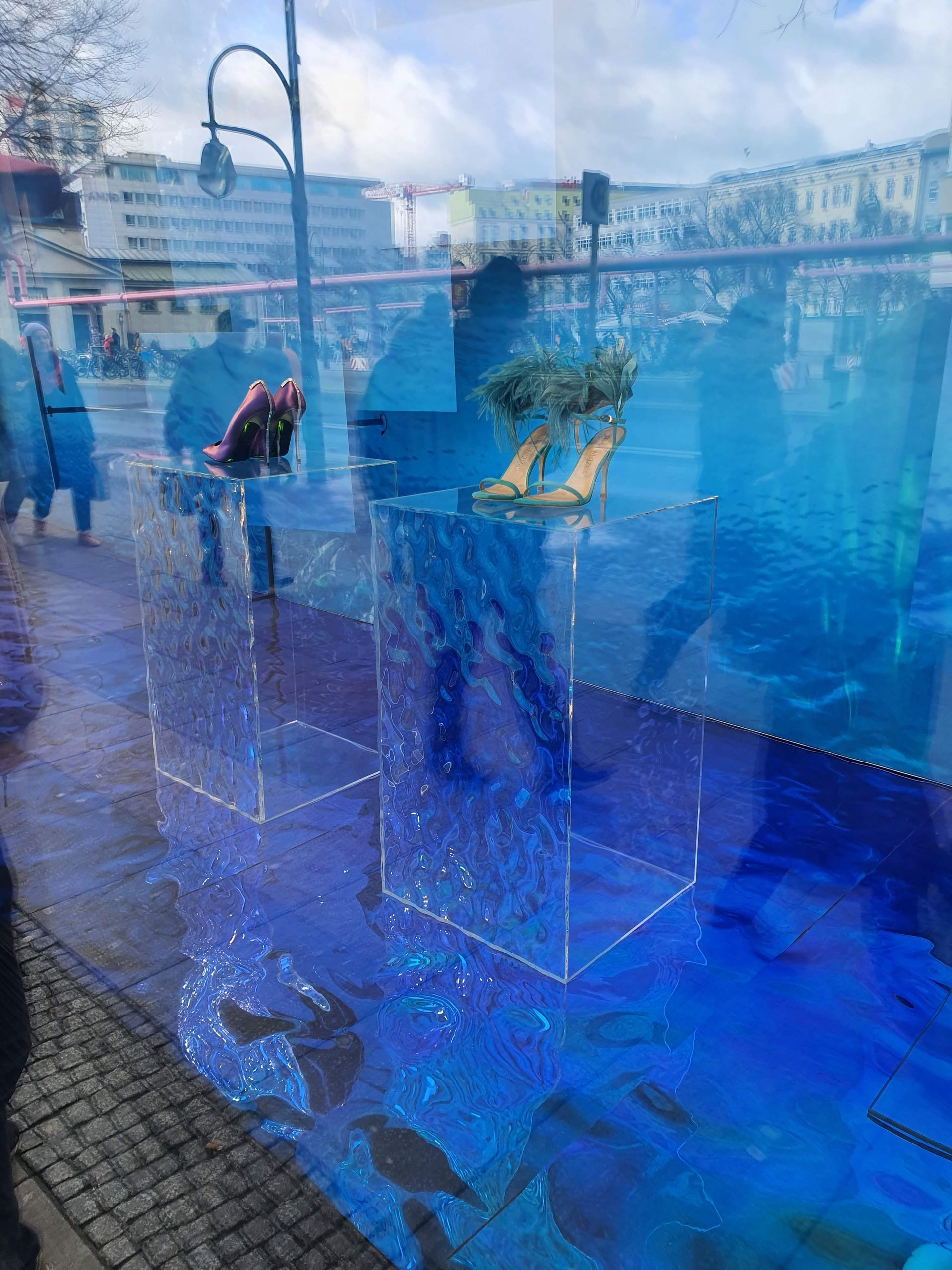 Spiegelnde Glasfläche mit Blick auf eine Straße und Schaufensterobjekte im Vordergrund.