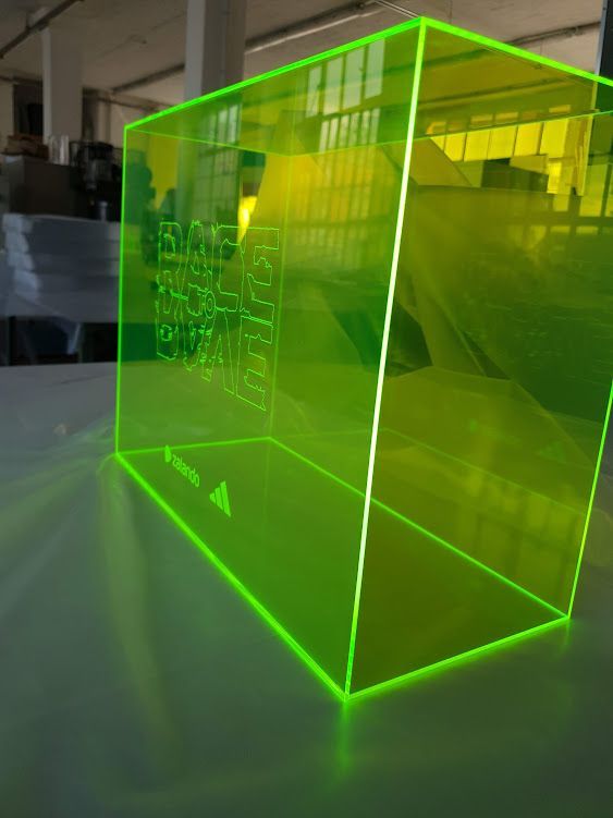 Leuchtend grünes, transparentes Kunststoffgehäuse in Würfelform in einer Werkstatt.