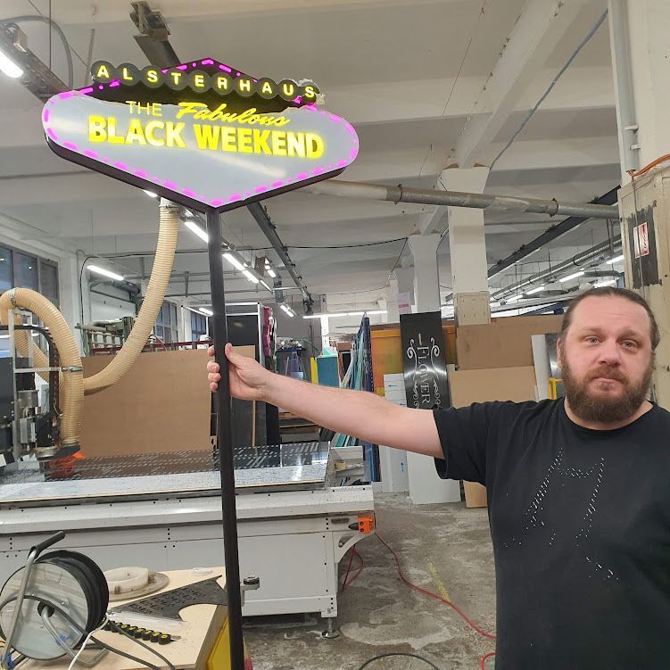 Leuchtendes Neon-Schild „BLACK WEEKEND“ hängt in einer Werkstatt, Person im Vordergrund.