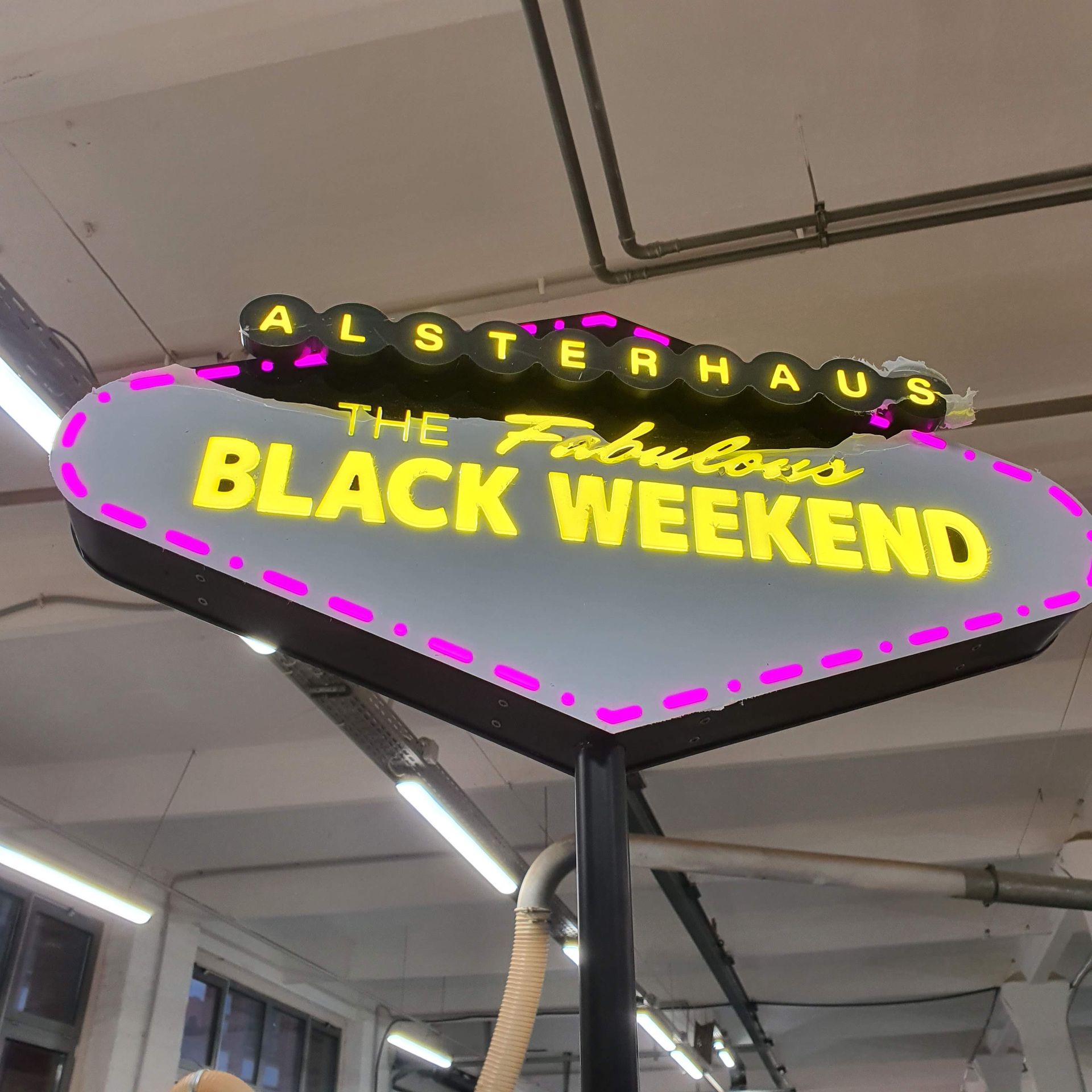 Neon-Leuchtschild „BLACK WEEKEND“ in Gelb und Pink, liegend auf dem Werkstattboden.