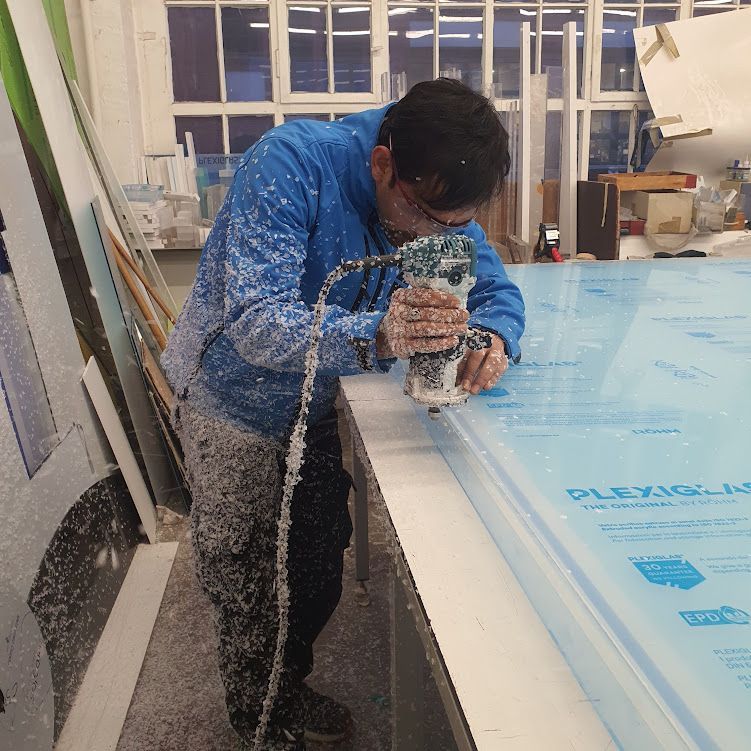 Mitarbeiter bearbeitet eine große Kunststoffplatte mit einem Handwerkzeug.