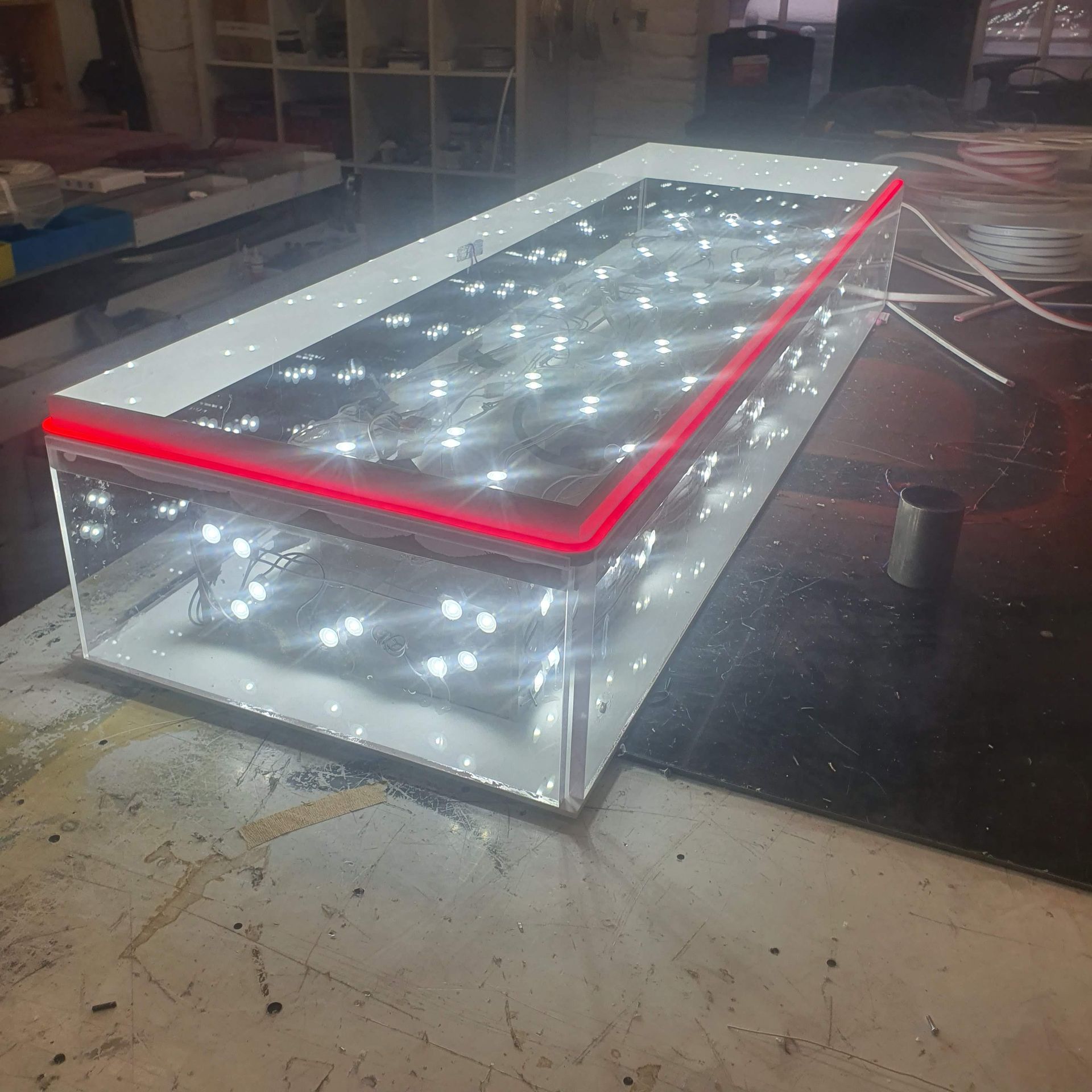 Quadratisches, mehrschichtiges Leuchtobjekt mit weißen LEDs und roter Kante in einer Werkstatt.