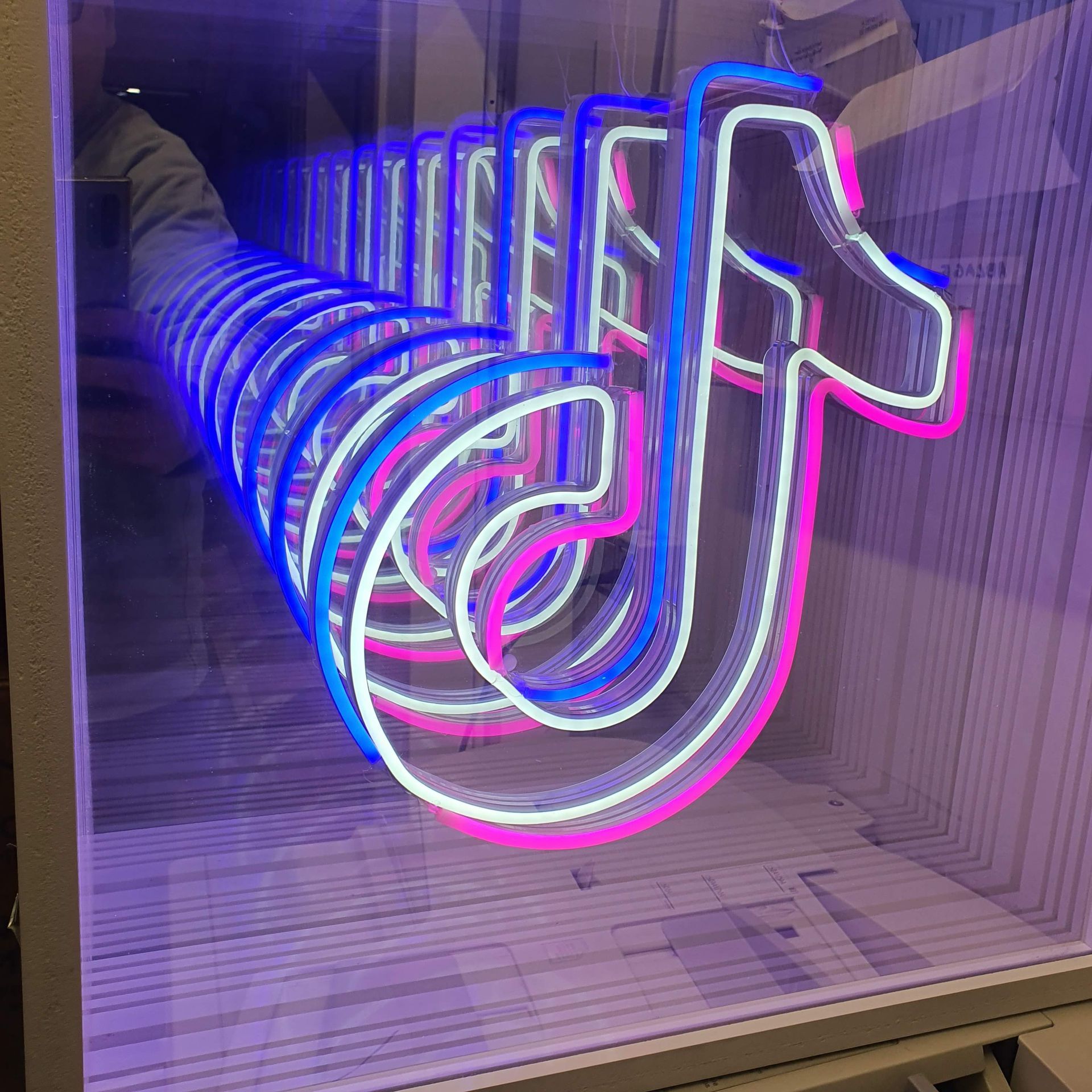 Leuchtende blaue Neon-Schrift in Form eines stilisierten TikTok-Logogs an einer Wand.