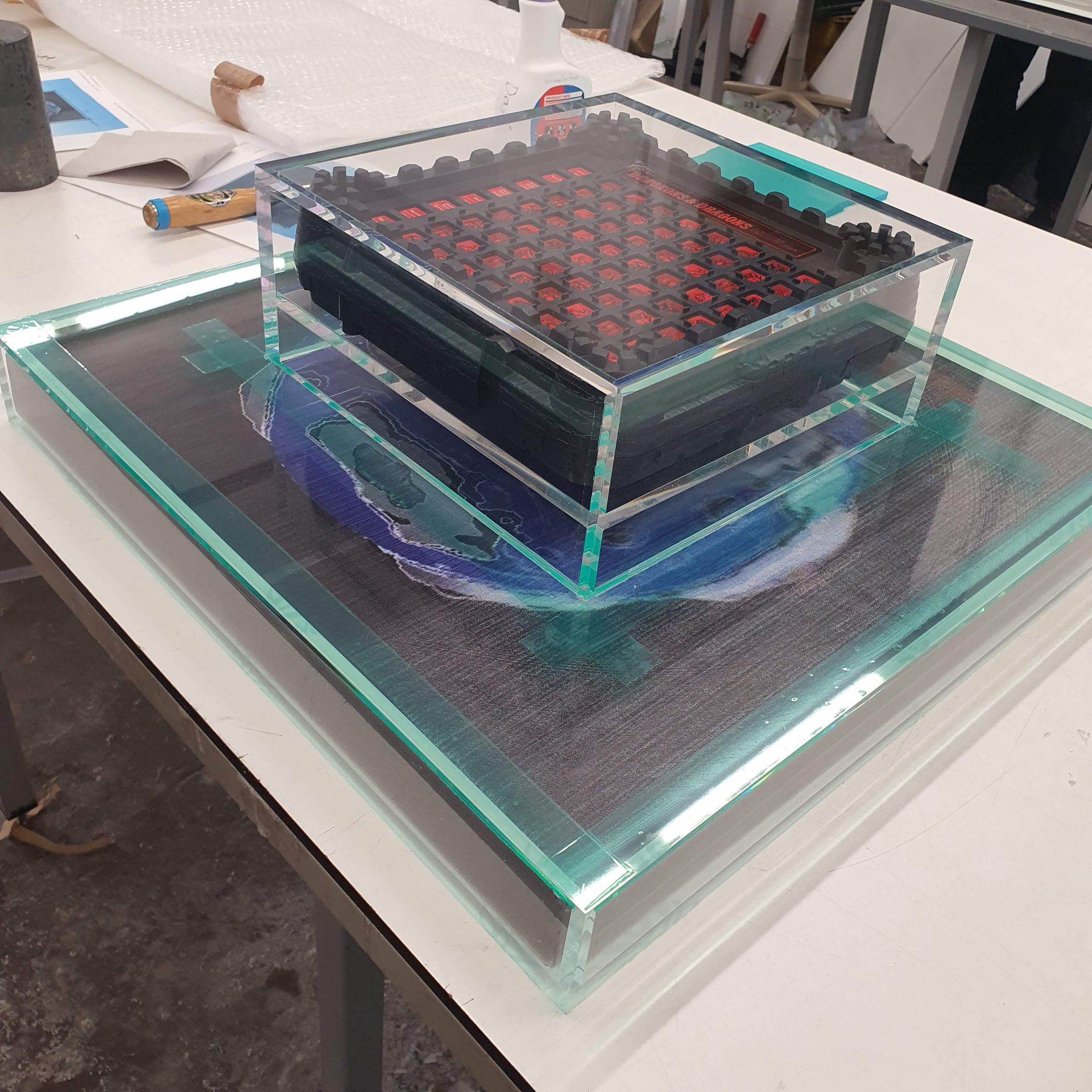 Mehrschichtiges, quadratisches Objekt aus transparentem Kunststoff mit roten Elementen im Inneren.