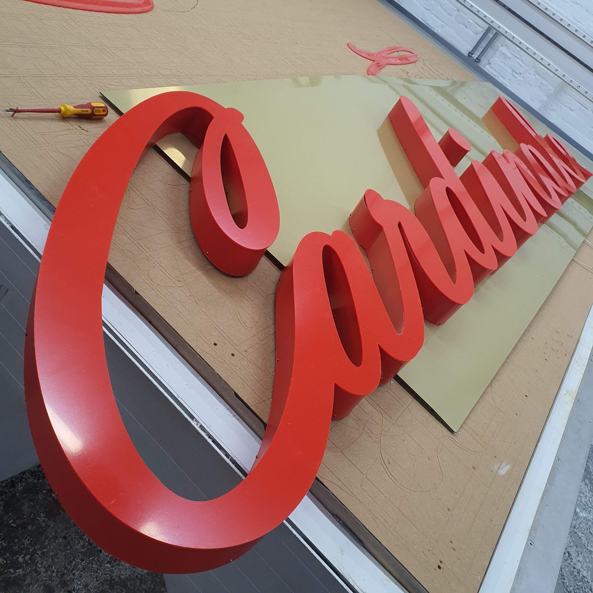 Roter, geschwungener Schriftzug aus Kunststoff oder Acryl, montiert auf einer Oberfläche.