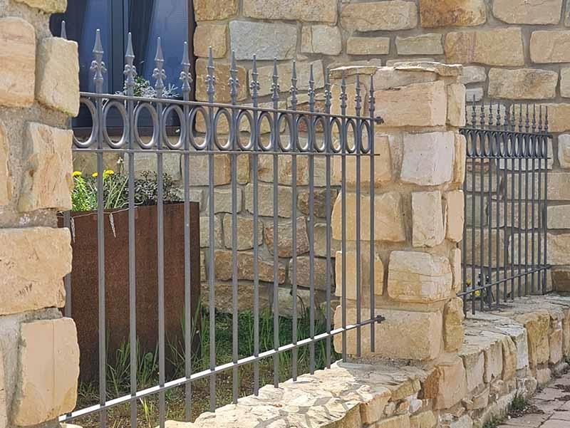 Eine Steinmauer mit einem schmiedeeisernen Zaun davor