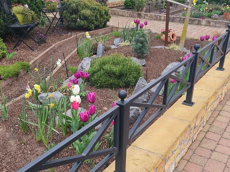 Ein Garten mit Blumen und einem Zaun darum herum.