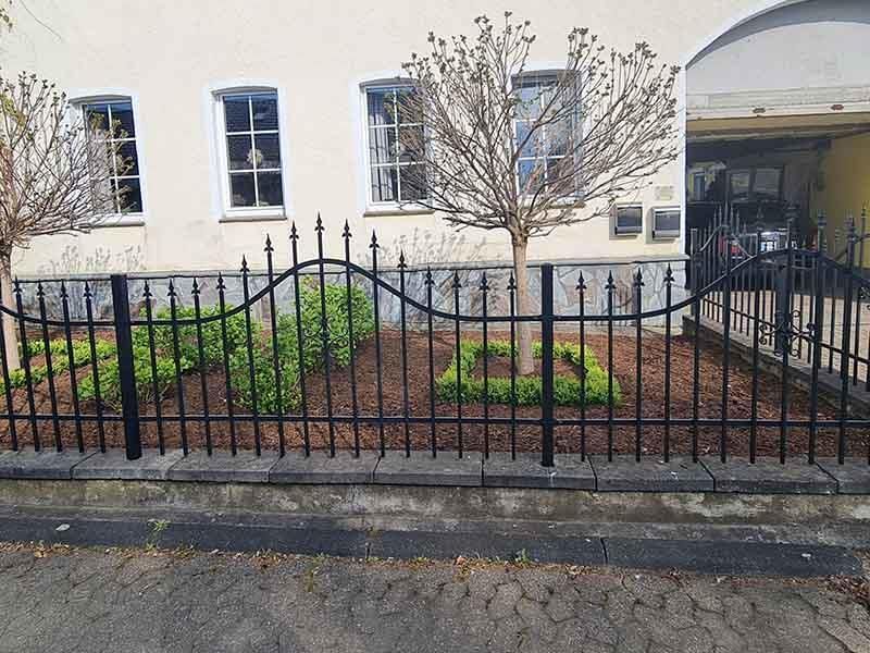 Ein schmiedeeiserner Zaun umgibt einen Garten vor einem Haus.