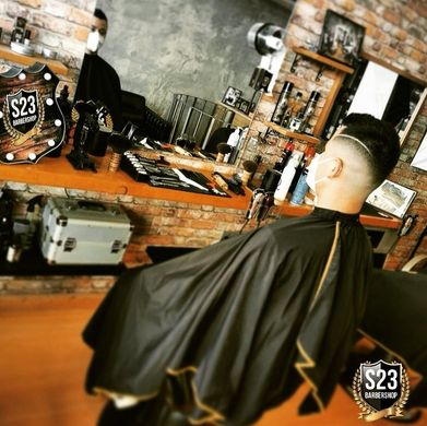 Un hombre se está cortando el pelo en una barbería con un cartel que dice s23